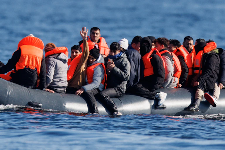 A large of men in orange life jackets crowded into a small dinghy, crossing the English channel