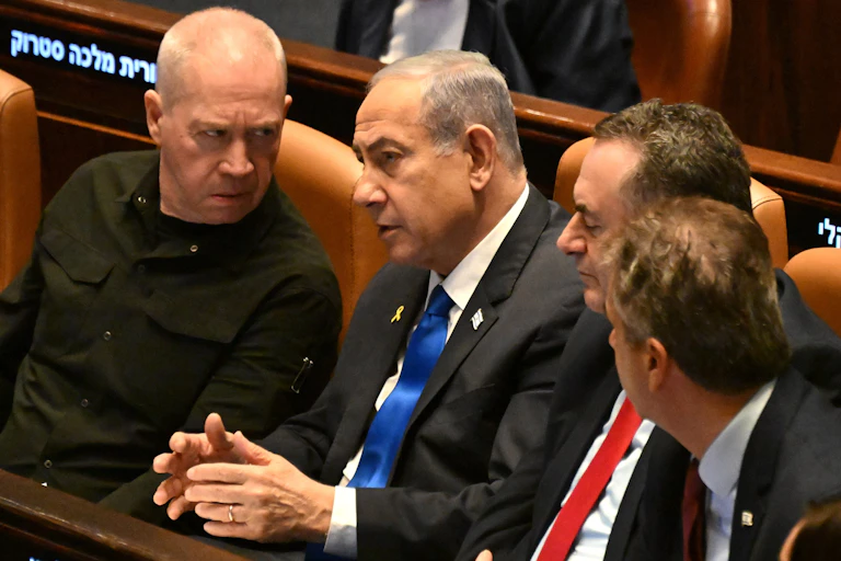 Yoav Gallant looking at Benjamin Netanyahu angrily as they sit next to each other.