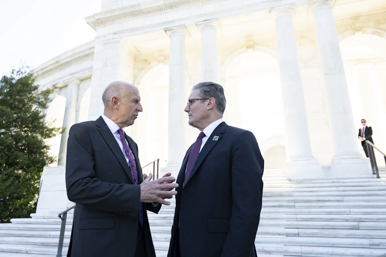 John Healey and Keir Starmer speaking to each other in front of a white columned structure at the US Arlington National Cemetery