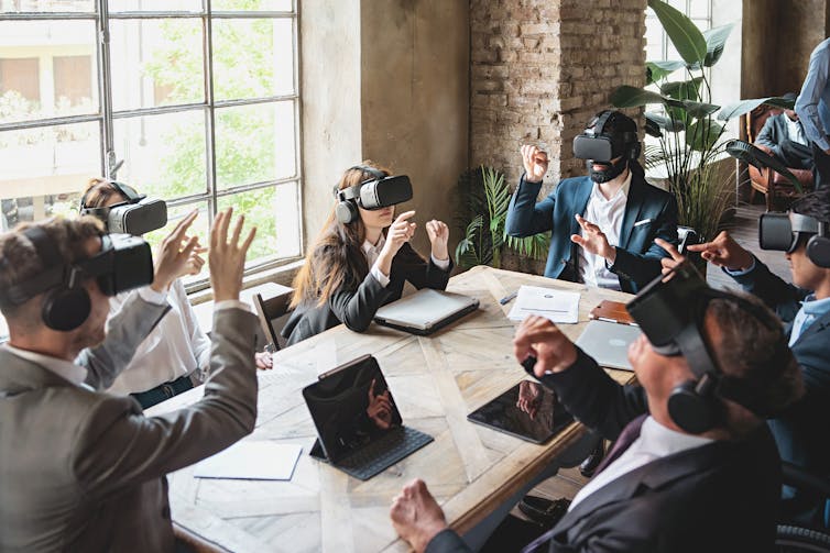 Group of people in suits wearing virtual reality headsets sit around a conference table
