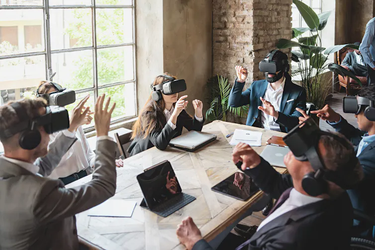 Group of people in suits wearing virtual reality headsets sit around a conference table