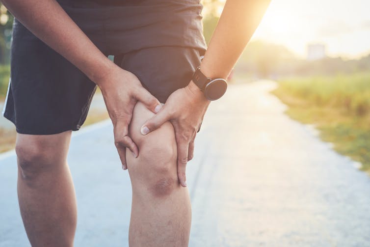 A man outdoors holding his knee.
