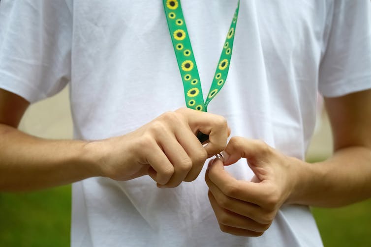 person in white tshirt wears a green lanyard with sunflowers on it
