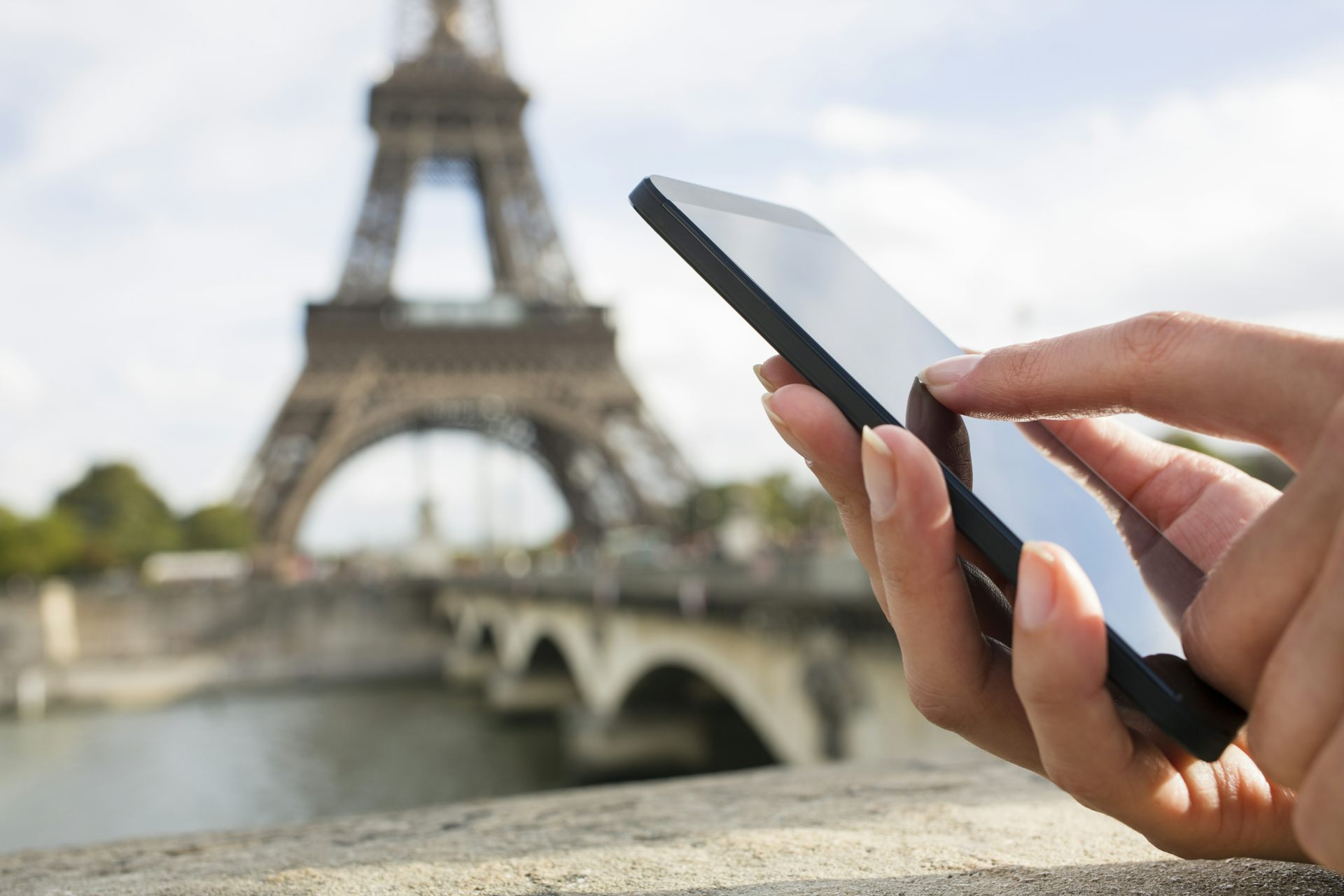 A hand holding a mobile phone with the Eiffel Tower in the background