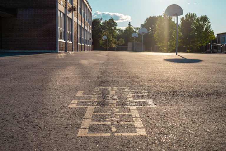 An empty school playground, with hopscotch and basketball courts.