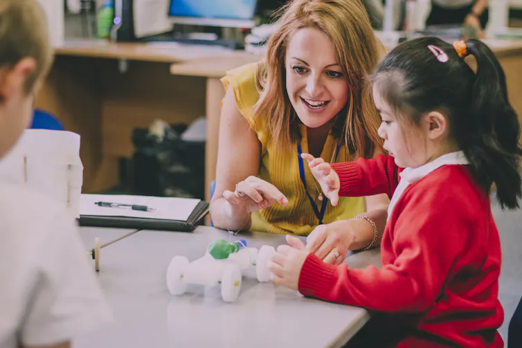 A teachers works with a young student at a desk.