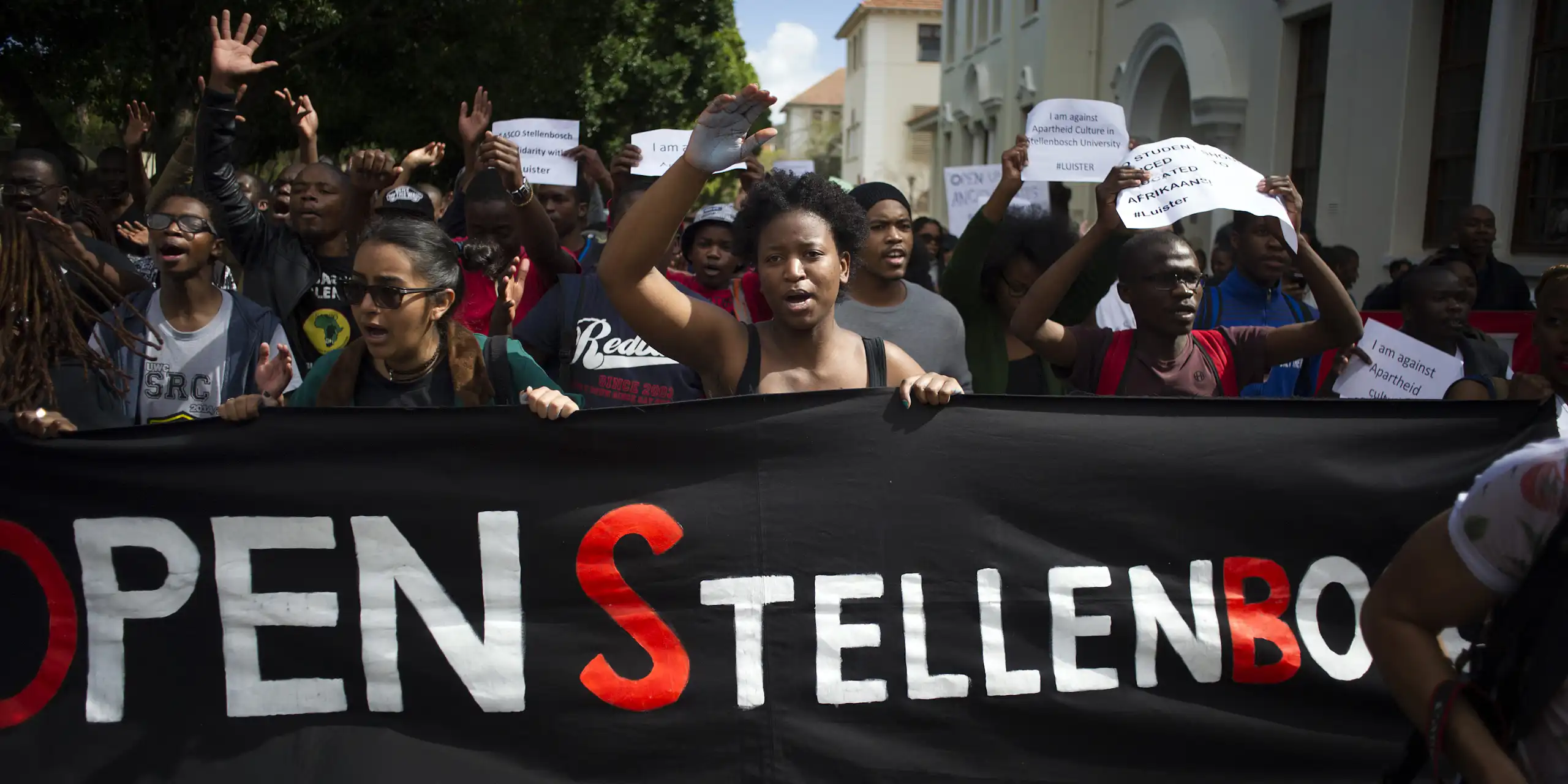 A group of protesters holding a banner that reads Open Stellenbosch. Others are holding placards calling for Afrikaans to be removed as a teaching language