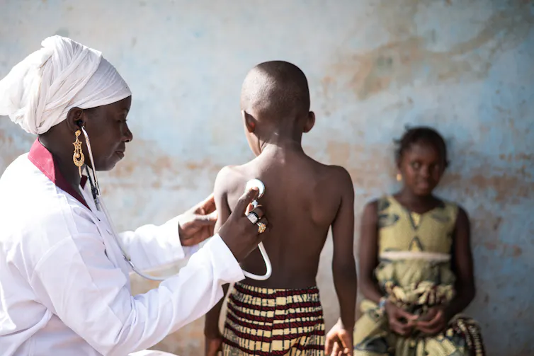 black doctor with stethoscope checking small child
