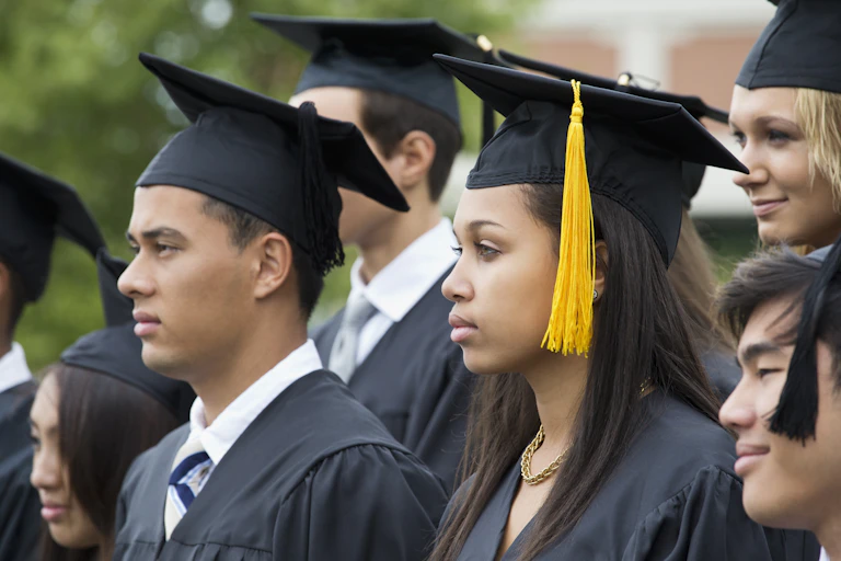 Several college students wearing caps and gowns look on at their graduation ceremony.