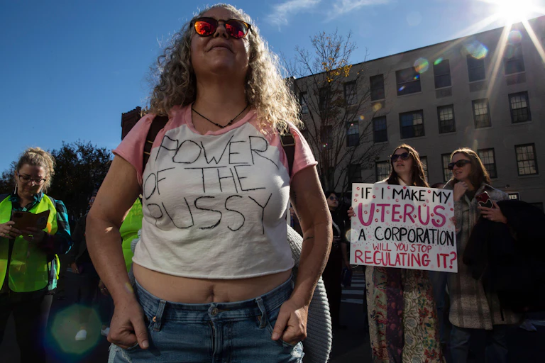 A women in a t-shirt reaidngt 'Power of the Pussy' demonstrates for reproductive rights with other women carrying signs.