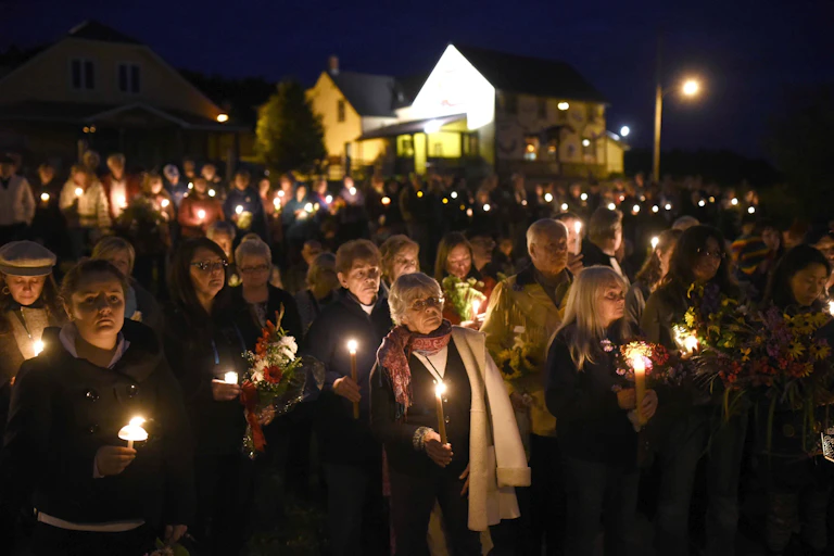 A group of mostly women hold candles at a night-time vigil.