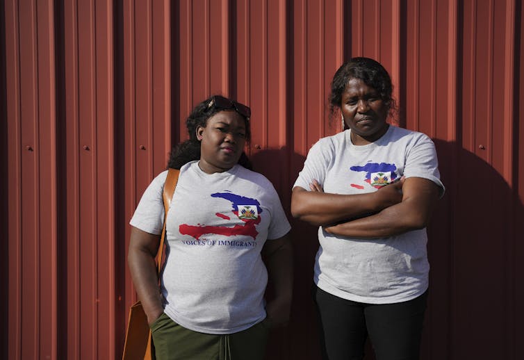 Two women from Haiti pose in front of a red wall.