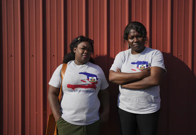 Two women from Haiti pose in front of a red wall.