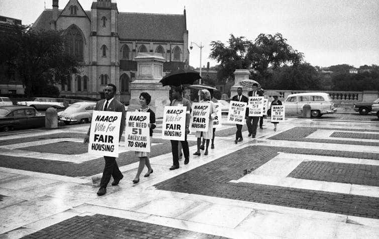 Black protestors hold picket signs in front of a building.
