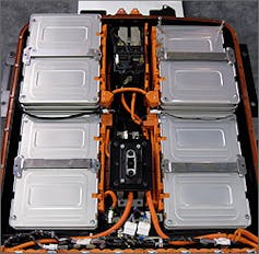 Flat silver batteries stacked in an array, connected by orange cables.