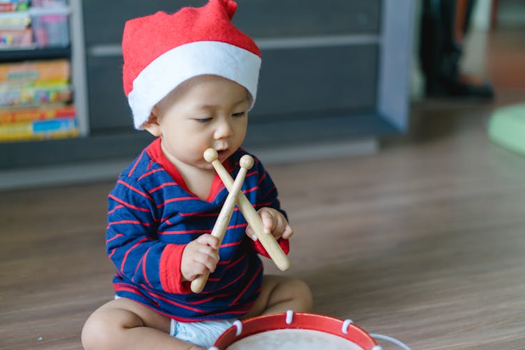 A baby in a Santa hat with a drum.
