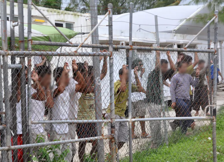 Asylum seekers stand behind a fence in Oscar compound at the Manus Island detention centre in Papua New Guinea, Friday, March 21, 2014.