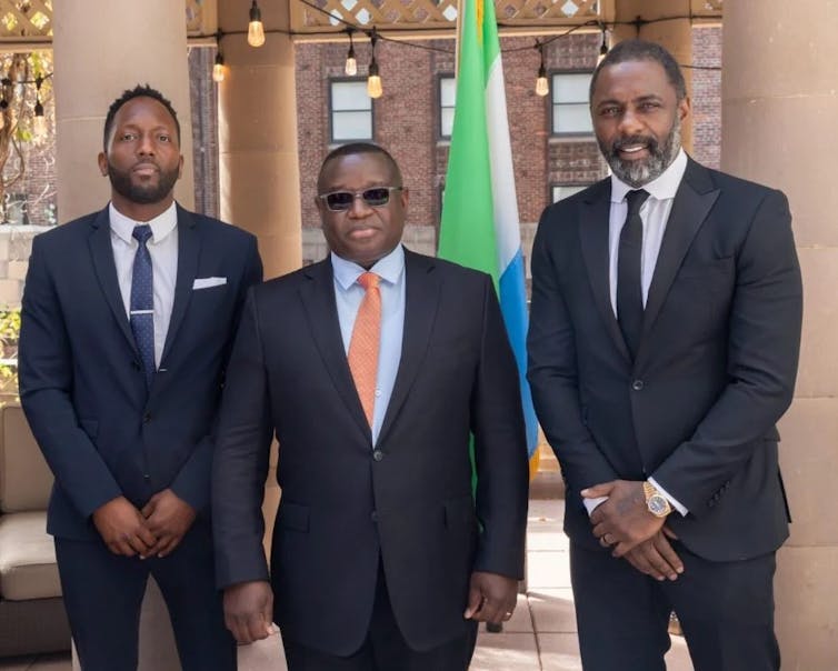 Idris Elba, Siaka Stevens and Julius Maada Bio in suits posing for a photograph.