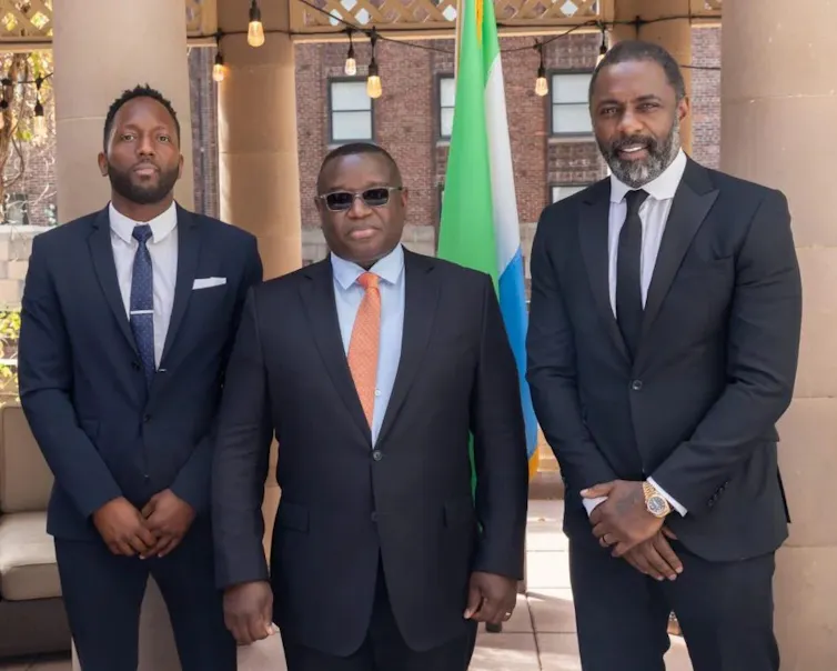 Idris Elba, Siaka Stevens and Julius Maada Bio in suits posing for a photograph.