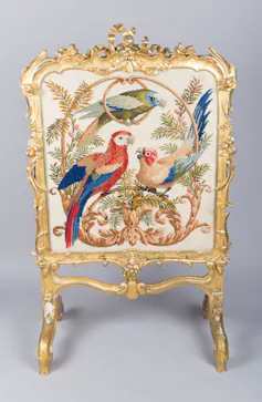 A gold decorative firescreen embroidered with parrots.
