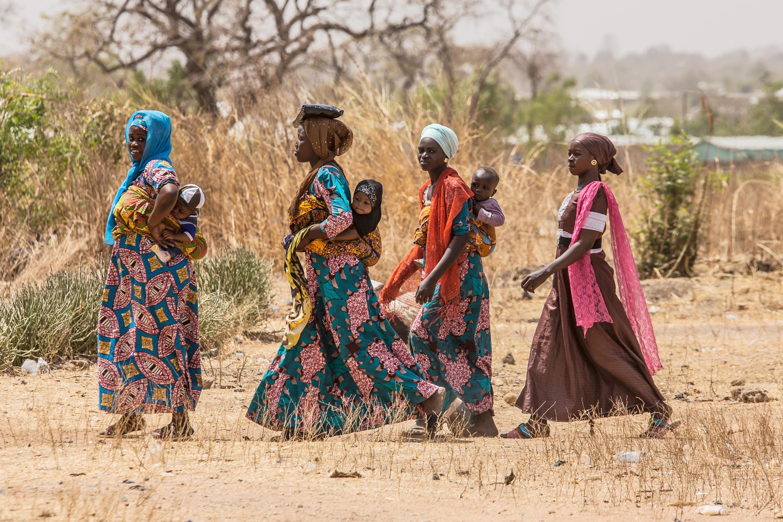 Four women walking, three of them with babies on their backs