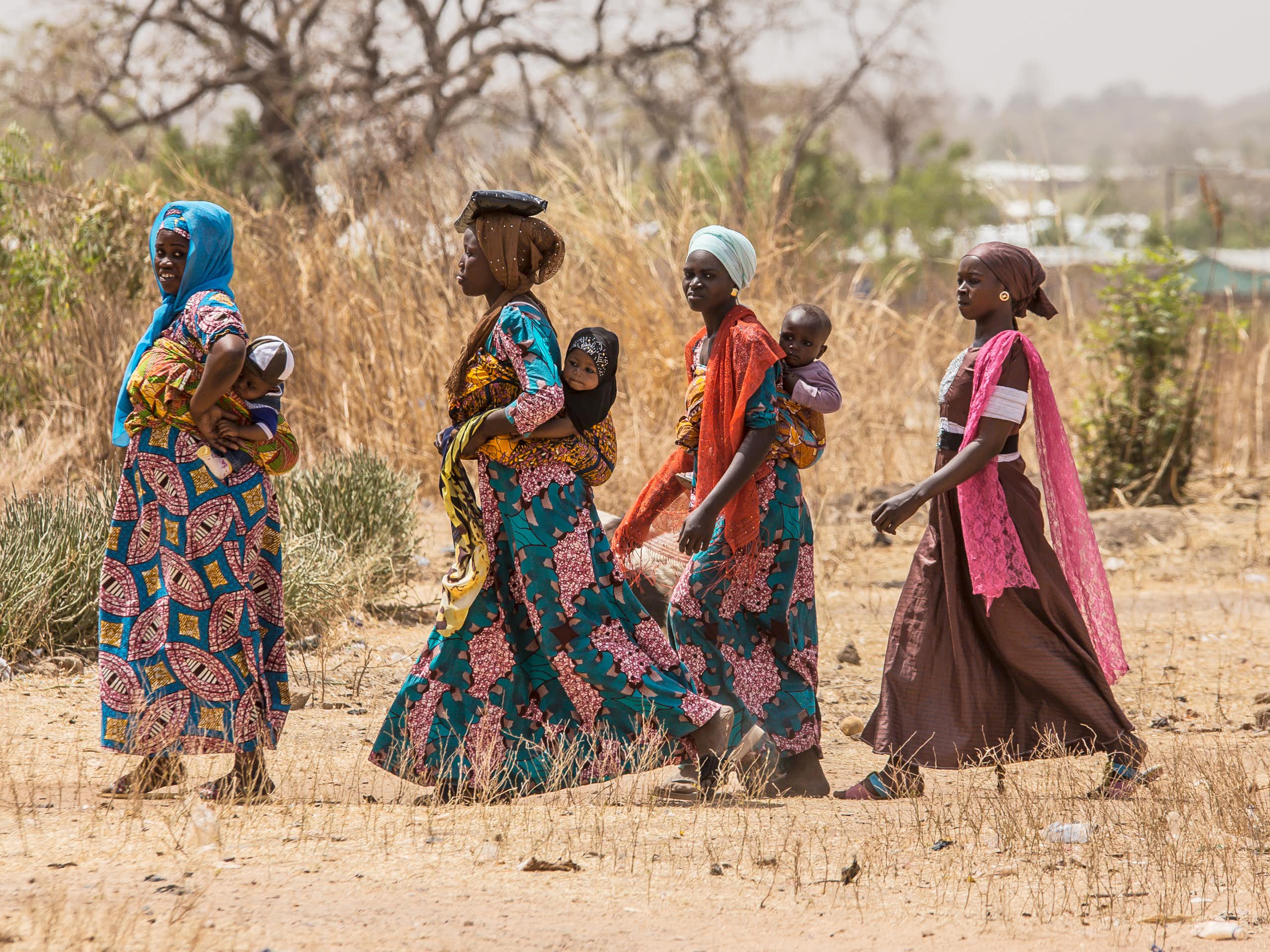Four women walking, three of them with babies on their backs