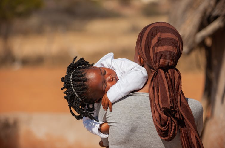Woman seen from the back, carrying a sleeping child
