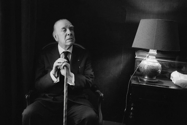 Black and white portrait of elderly man wearing suit and sitting in chair while clasping a cane with both hands.