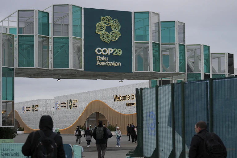 A group of people walk towards a building with a sign and logo for COP29