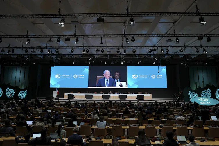 People sit at tables while a man gives a sppech at a podium.