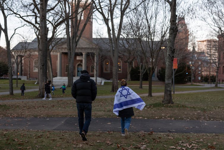 A woman draped in an Israeli flag and a man walk across a green toward a large brick building.