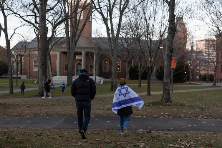 A woman draped in an Israeli flag and a man walk across a green toward a large brick building.