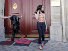 Une femme torse nu se tient devant une porte. Des mots sont écrits sur son corps