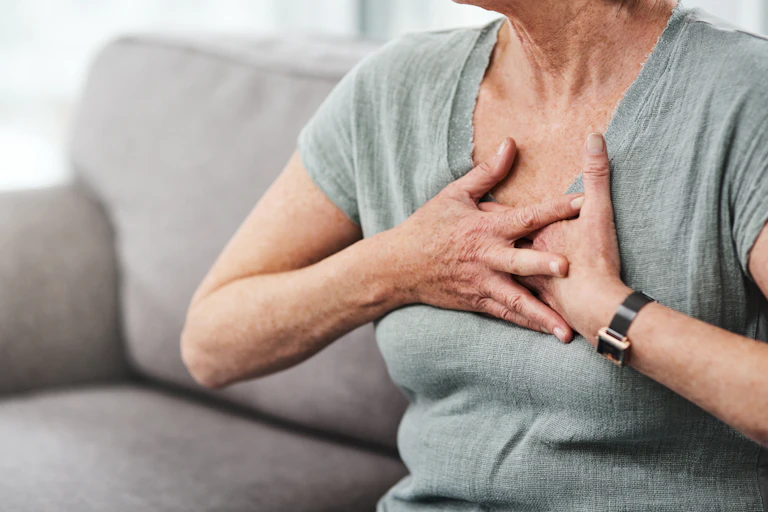A woman with her face cropped out of frame sitting on a sofa holding her hands to her chest