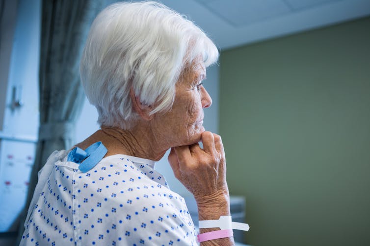 A woman with white hair in a hospital gown, looking away from the camera