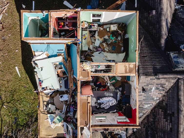 A tornado-damaged home seen from above with the roof missing and belongings strewn about in the rooms. The rooms look like colored boxes.