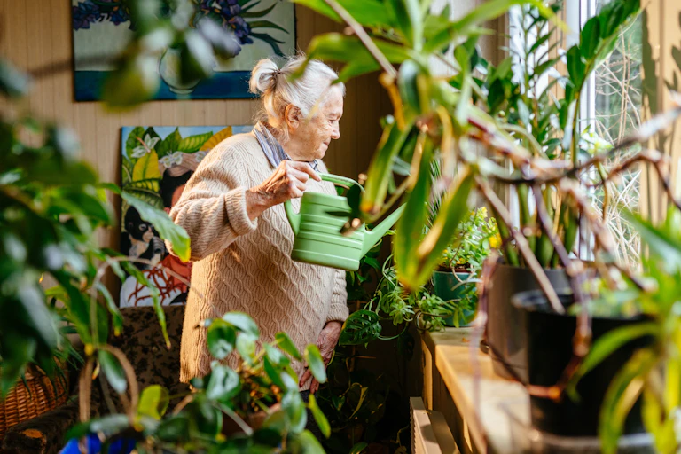 An older woman waters her plants