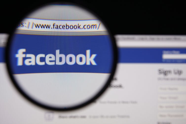 Photo of Facebook homepage on a monitor screen through a magnifying glass.