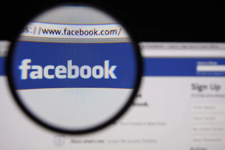 Photo of Facebook homepage on a monitor screen through a magnifying glass.