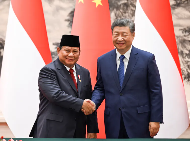 Two men shake hands in front of red and white flags.