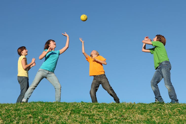 Four kids on a sunny day playing with a ball outdoors.