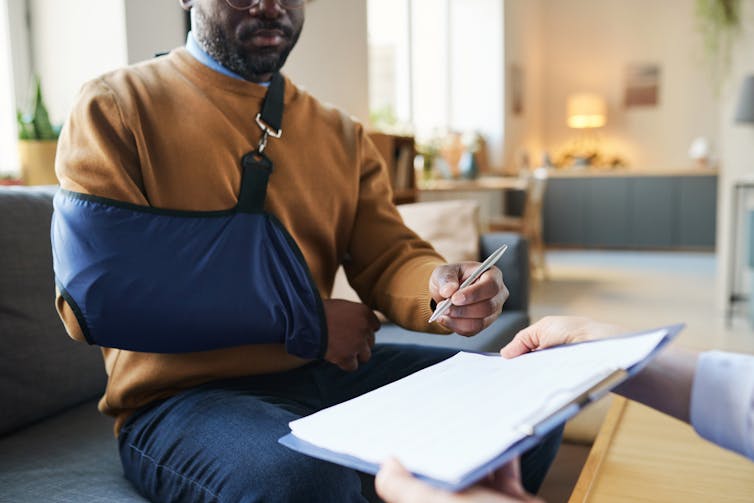 Man with arm in sling signing medical form on clipboard