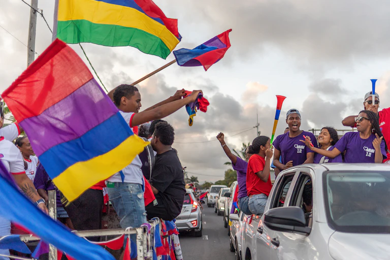 People wave flags and blow plastic horns in a line of cars