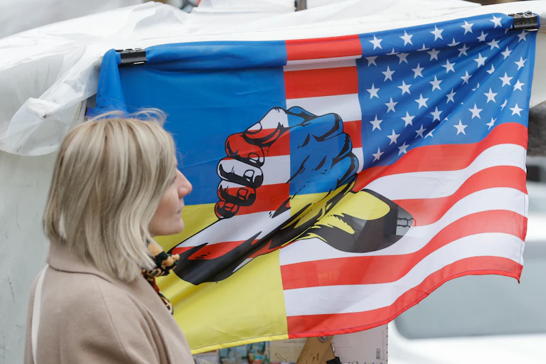 Woman walks past a flag made of the US and Ukrainian flags with two fists shaking hands