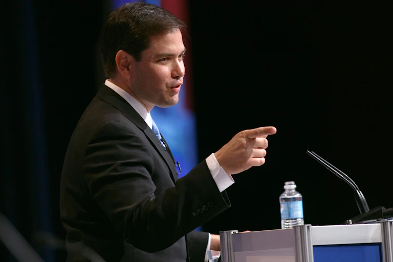 Marco Rubio in a suit with a finger pointed out.