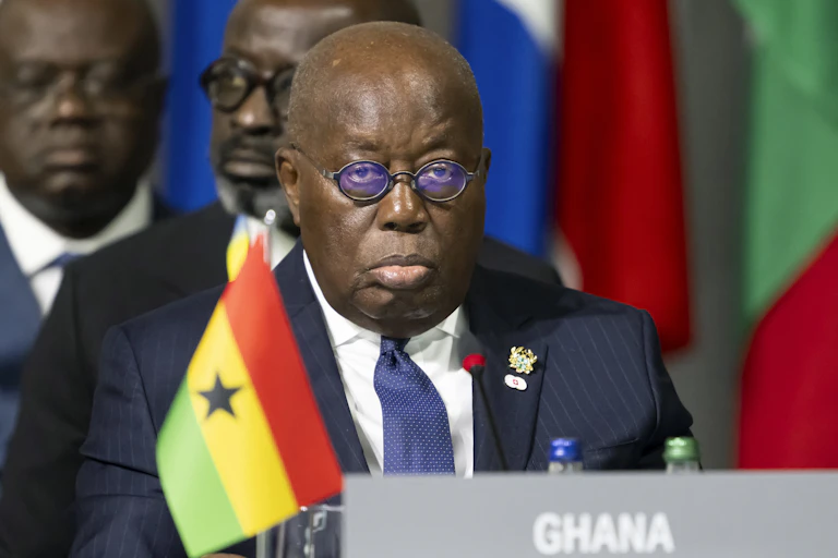 A man in suit and tie and spectacles, with a red. yellow and green flag in front of him
