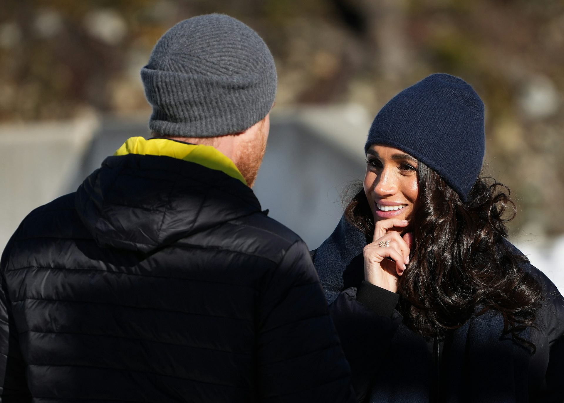 A dark haired woman in a winter toque smiles as she looks up at a red-haired man with his back to the camera.