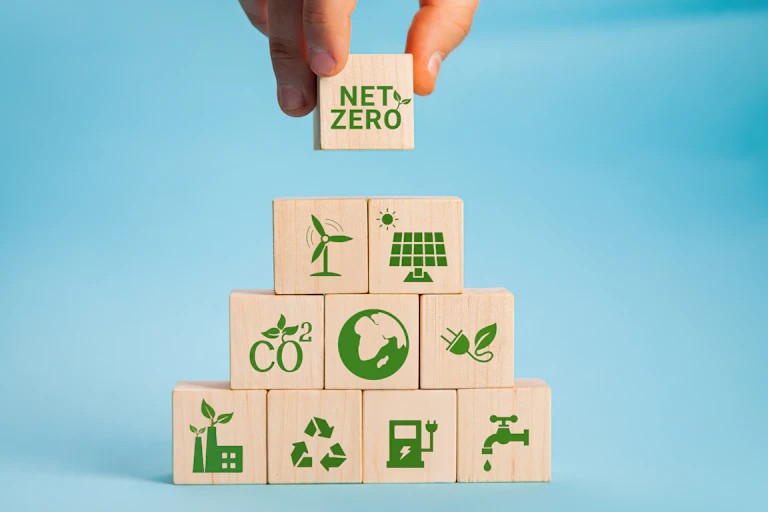 wooden blocks with green eco logos, hald lifting one block with net zero, blue background