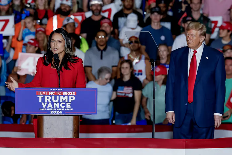 Republican poiltician Tulsi Gabbard speaks at a Trump campaign rally as Donald Trump watches from the side.