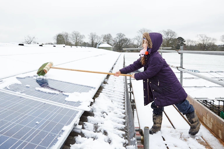 A girl sweeping snow off rooftop solar panels.